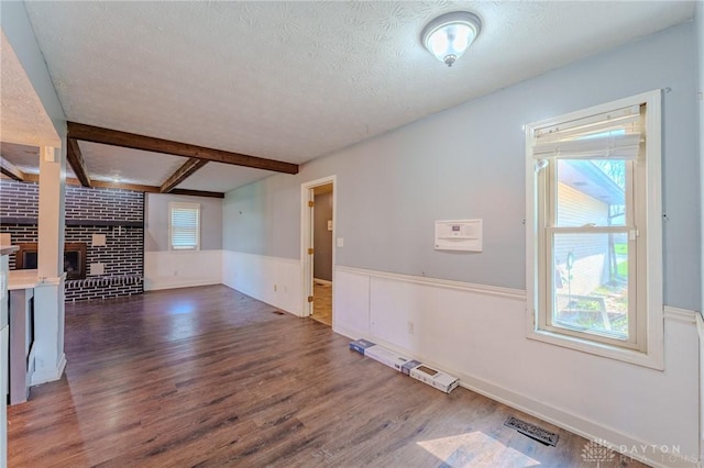 unfurnished living room with wood finished floors, wainscoting, a fireplace, visible vents, and a textured ceiling