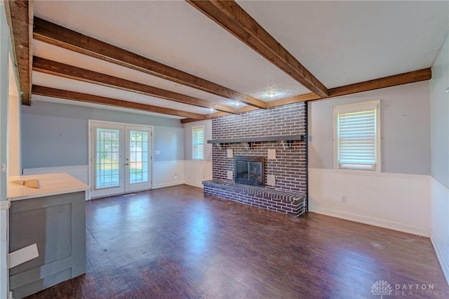 unfurnished living room with beam ceiling, wood finished floors, french doors, and a brick fireplace