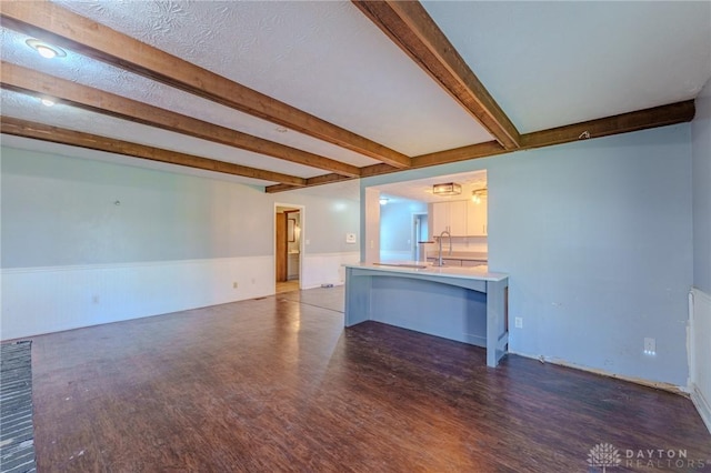 unfurnished living room with beamed ceiling, wainscoting, and wood finished floors