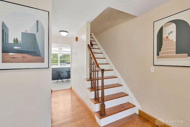 stairway with baseboards, wood finished floors, and arched walkways
