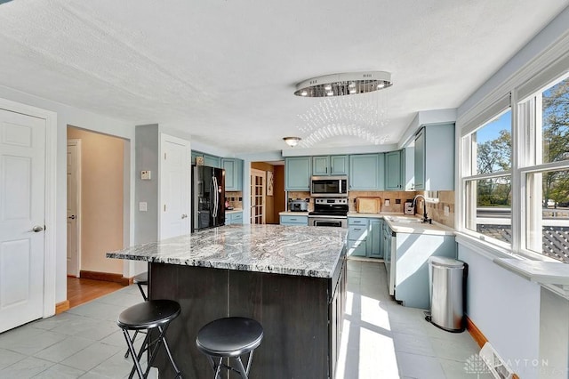 kitchen featuring light stone counters, decorative backsplash, appliances with stainless steel finishes, a sink, and a kitchen breakfast bar