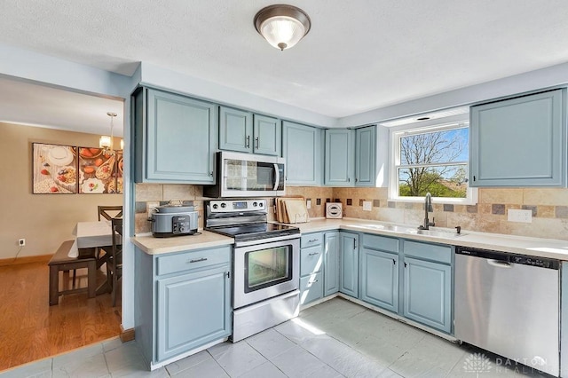 kitchen featuring a sink, appliances with stainless steel finishes, backsplash, light countertops, and blue cabinets