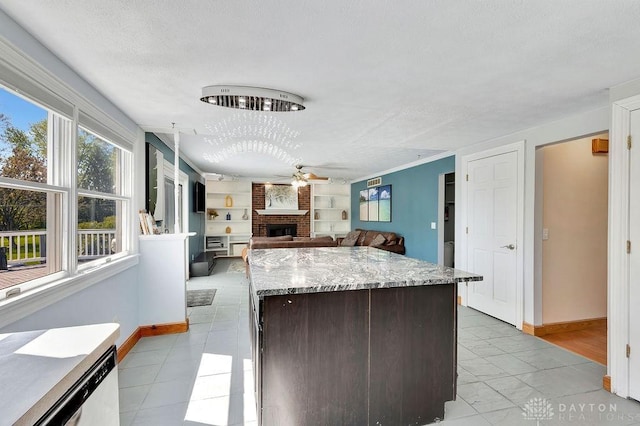 kitchen with a fireplace, ceiling fan, a kitchen island, and baseboards