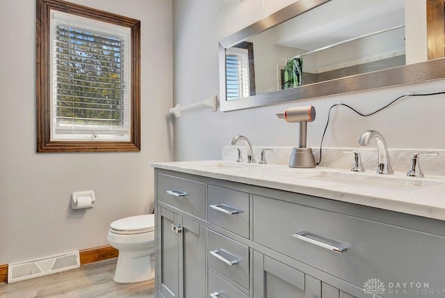 bathroom with wood finished floors, toilet, a sink, baseboards, and visible vents