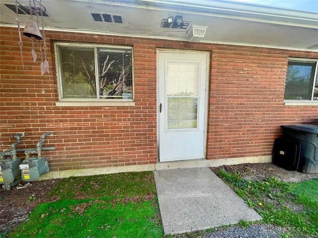 view of exterior entry featuring visible vents and brick siding