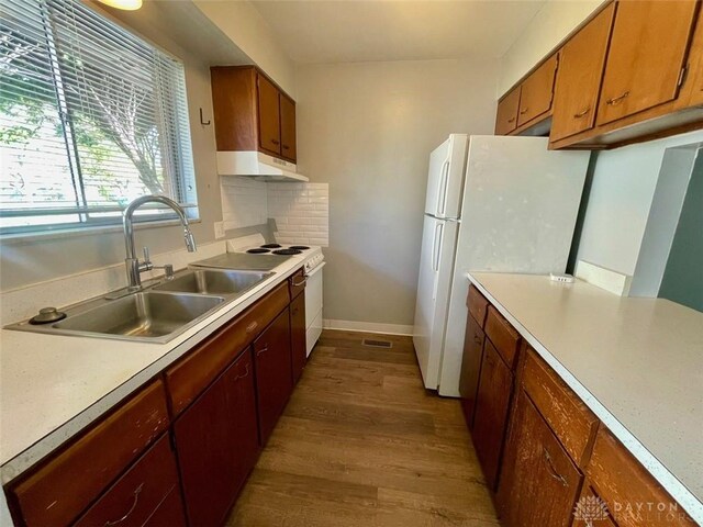 kitchen featuring a sink, light countertops, under cabinet range hood, wood finished floors, and white appliances