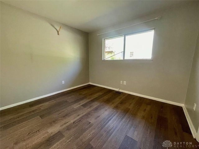 unfurnished room with dark wood-type flooring, visible vents, and baseboards
