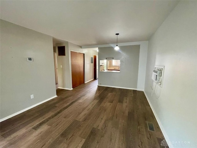 unfurnished dining area with dark wood-type flooring, visible vents, a wall unit AC, and baseboards