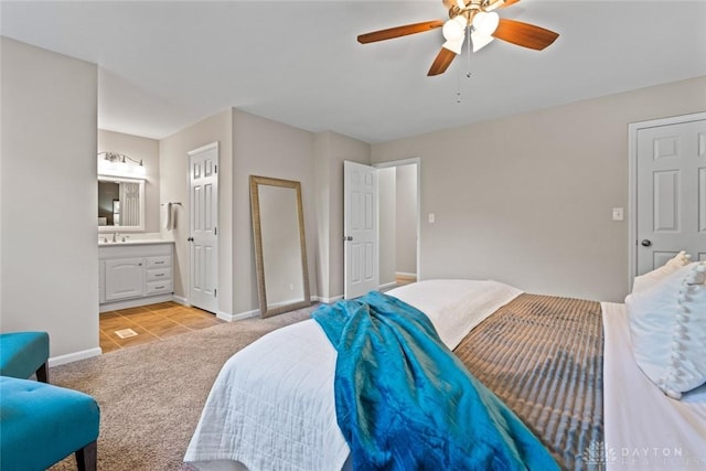 bedroom featuring ensuite bath, light tile patterned floors, light carpet, a sink, and baseboards
