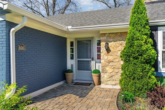 entrance to property featuring brick siding, a shingled roof, and stone siding