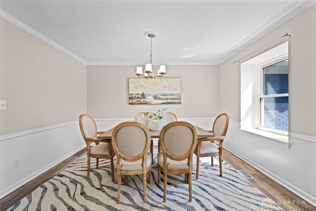 dining area with an inviting chandelier, wood finished floors, visible vents, and ornamental molding