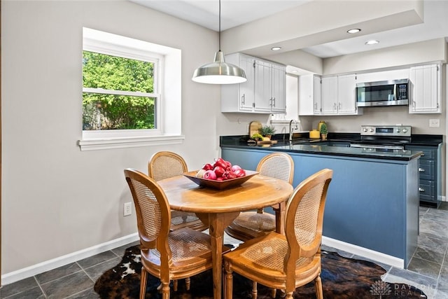 kitchen with a sink, baseboards, dark countertops, white cabinets, and appliances with stainless steel finishes