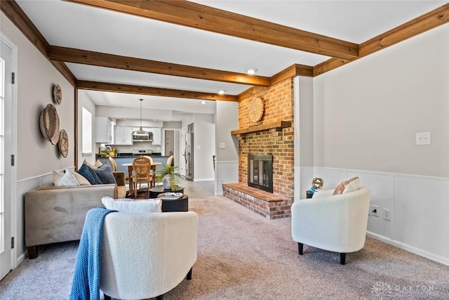 living area with beam ceiling, a fireplace, a wainscoted wall, and light carpet