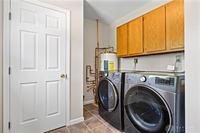 clothes washing area featuring washing machine and clothes dryer, baseboards, electric water heater, cabinet space, and dark tile patterned floors