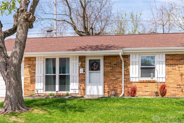 view of front of house featuring brick siding, a front lawn, and roof with shingles