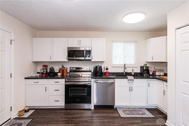 kitchen featuring a sink, stainless steel appliances, dark wood-type flooring, dark countertops, and white cabinets