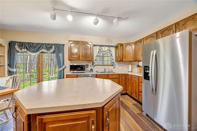 kitchen with a sink, brown cabinetry, light countertops, appliances with stainless steel finishes, and wood finished floors