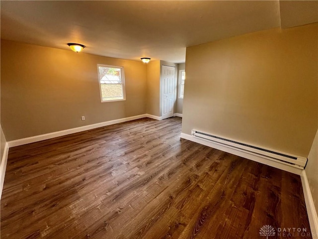 empty room featuring baseboard heating, baseboards, and dark wood-style floors