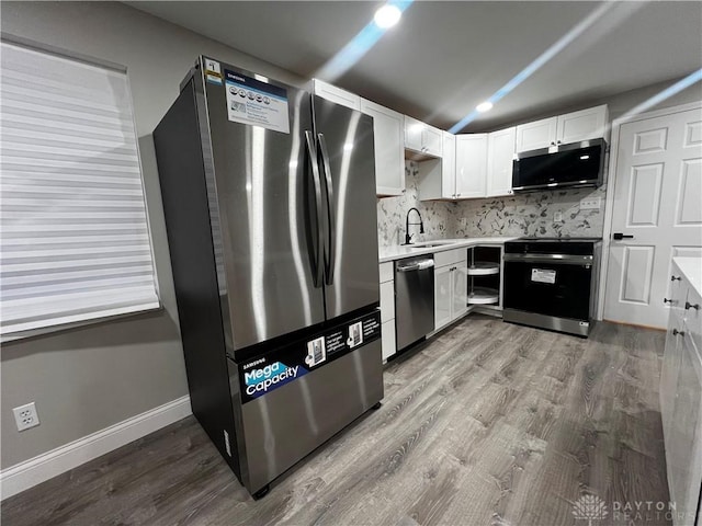 kitchen featuring wood finished floors, decorative backsplash, stainless steel appliances, light countertops, and white cabinets