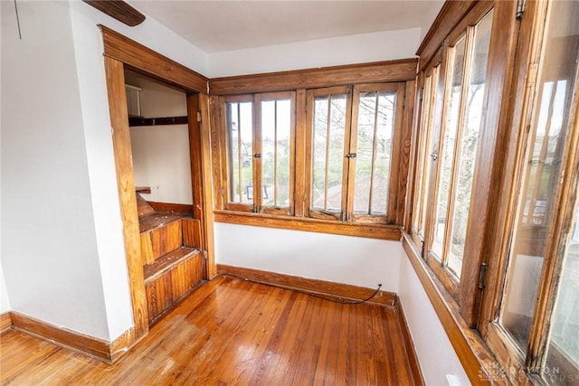 unfurnished sunroom featuring baseboards, a wealth of natural light, french doors, and wood-type flooring