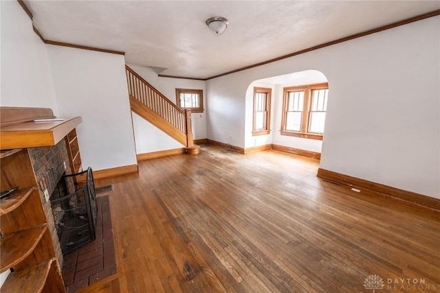 unfurnished living room featuring stairway, crown molding, baseboards, arched walkways, and hardwood / wood-style flooring
