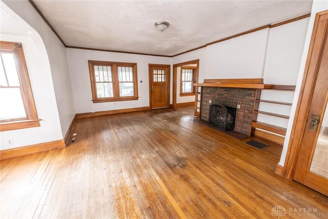 unfurnished living room with a fireplace, wood-type flooring, crown molding, visible vents, and baseboards