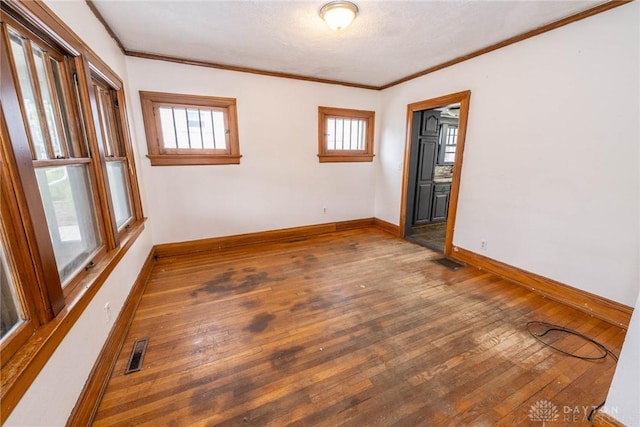 unfurnished room with visible vents, hardwood / wood-style floors, ornamental molding, and baseboards