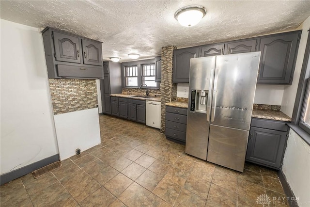 kitchen featuring a textured ceiling, white dishwasher, stainless steel fridge, and a sink