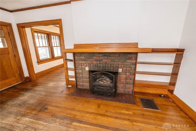 unfurnished living room featuring visible vents, baseboards, ornamental molding, a brick fireplace, and wood finished floors