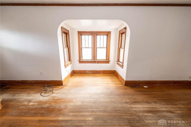 unfurnished room featuring hardwood / wood-style floors, baseboards, and arched walkways