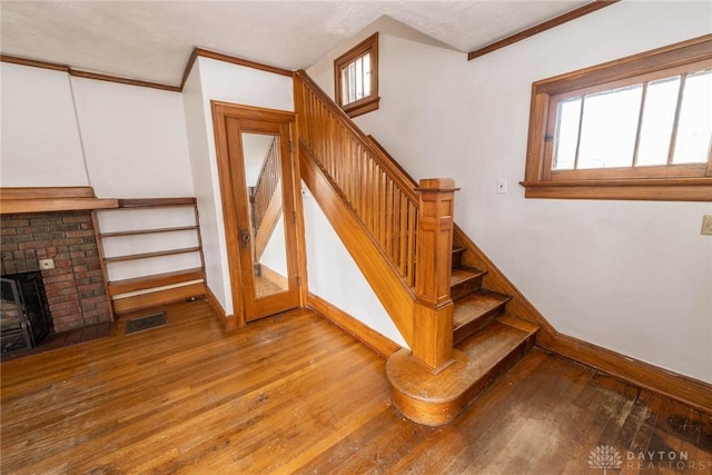 stairs with wood finished floors, visible vents, crown molding, and baseboards