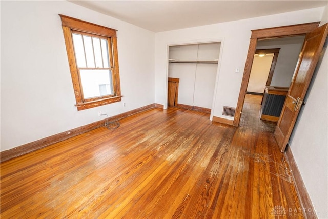 unfurnished bedroom featuring visible vents, a closet, baseboards, and wood-type flooring