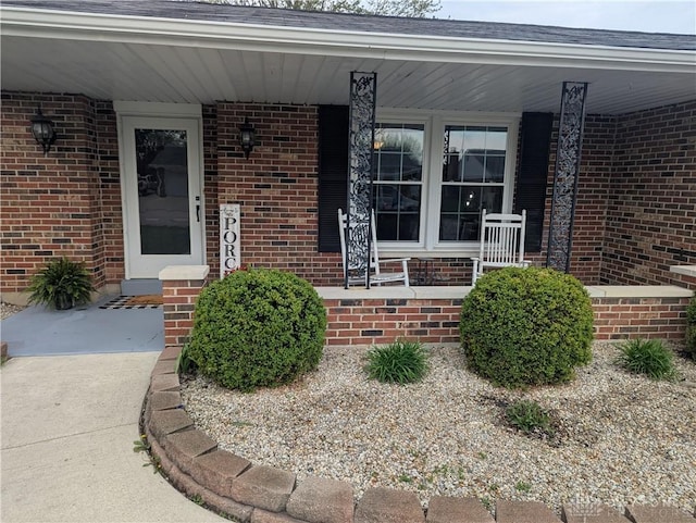 view of exterior entry with brick siding and a porch