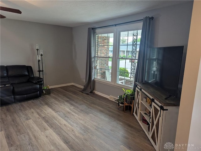 living area with wood finished floors, a ceiling fan, visible vents, and baseboards