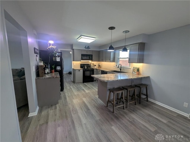 kitchen with a sink, black appliances, light wood-style flooring, a peninsula, and gray cabinetry