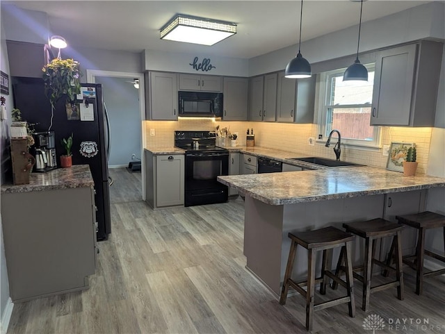 kitchen featuring a breakfast bar area, a sink, gray cabinetry, black appliances, and a peninsula