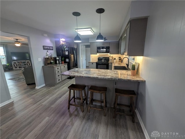kitchen featuring a sink, black appliances, a peninsula, gray cabinetry, and wood finished floors