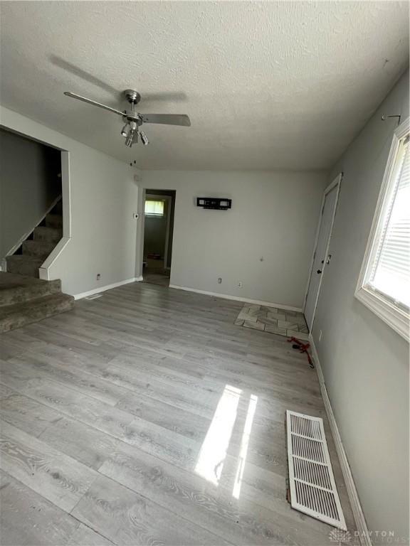 unfurnished living room with a textured ceiling, visible vents, ceiling fan, and baseboards