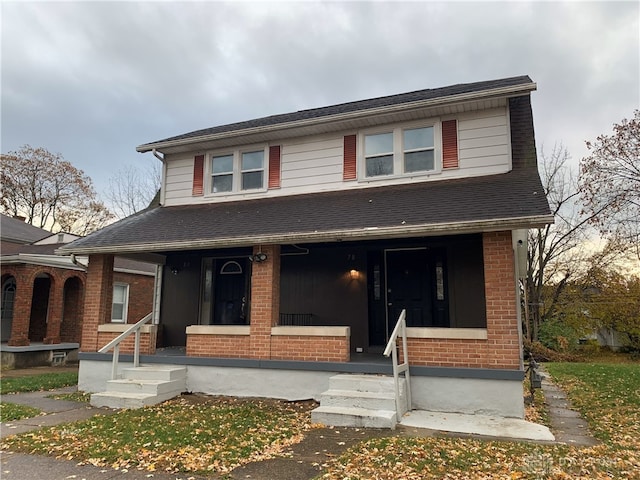 view of front of house with a porch, brick siding, and roof with shingles