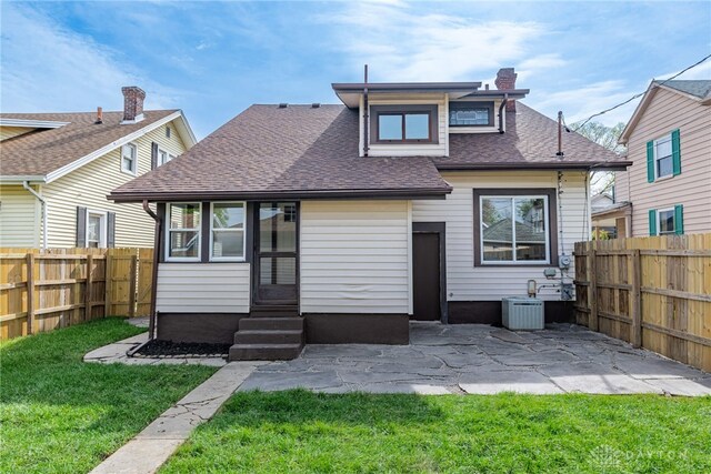 back of property with a chimney, a fenced backyard, a yard, entry steps, and roof with shingles