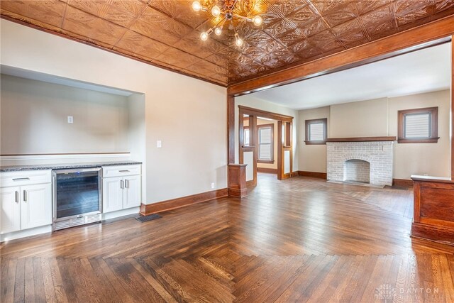 unfurnished living room featuring a chandelier, a fireplace, an ornate ceiling, baseboards, and beverage cooler
