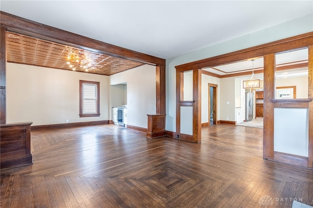 unfurnished living room with crown molding, a notable chandelier, and baseboards