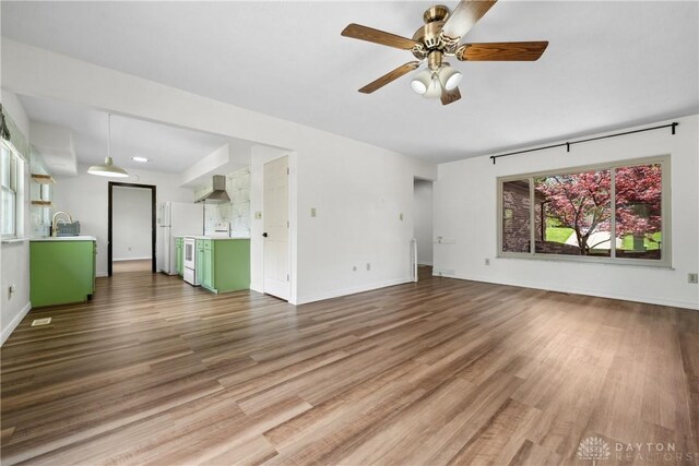 unfurnished living room with baseboards, wood finished floors, ceiling fan, and a sink