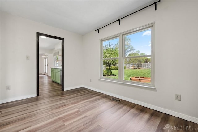 empty room with wood finished floors, visible vents, and a healthy amount of sunlight