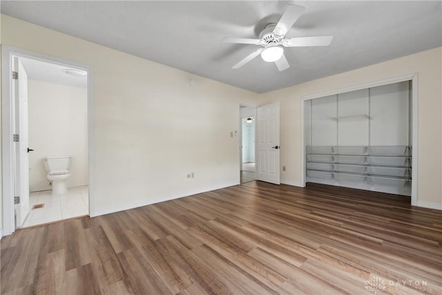 unfurnished bedroom with wood finished floors, ensuite bathroom, baseboards, and a closet