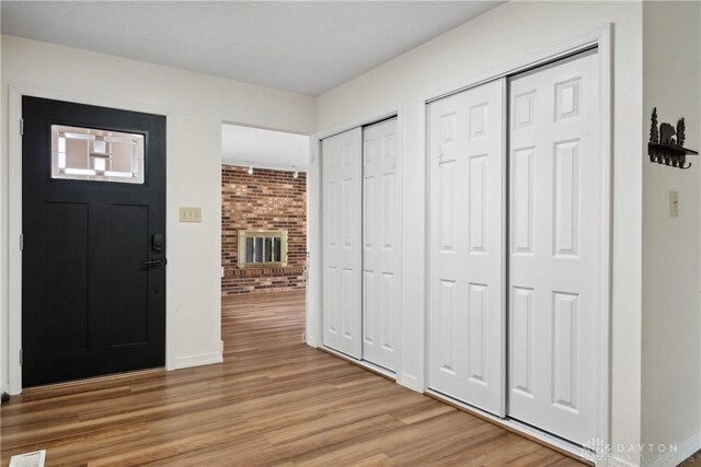 entrance foyer featuring baseboards, light wood-style floors, and a brick fireplace