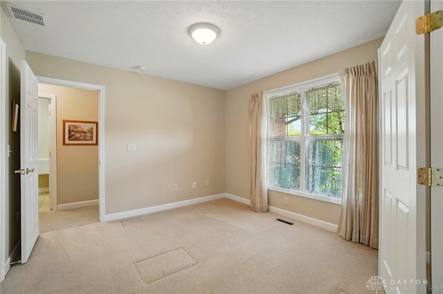 empty room with baseboards, visible vents, and light colored carpet