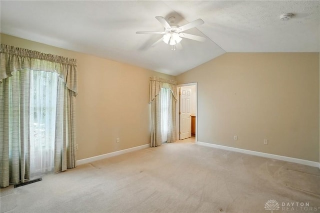 empty room with light colored carpet, vaulted ceiling, baseboards, visible vents, and a ceiling fan