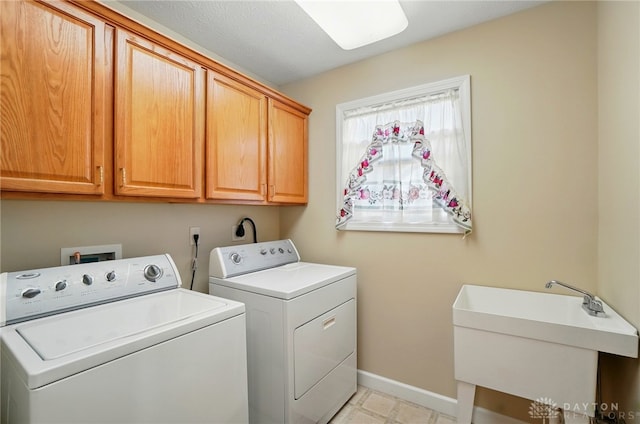 washroom with a sink, cabinet space, washing machine and clothes dryer, and baseboards