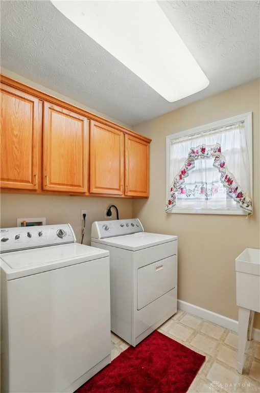 laundry area featuring baseboards, cabinet space, washing machine and clothes dryer, and a textured ceiling